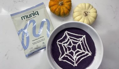 A picture of a blueberry smoothie bowl with a white spiderweb topping with pumpkins in the background