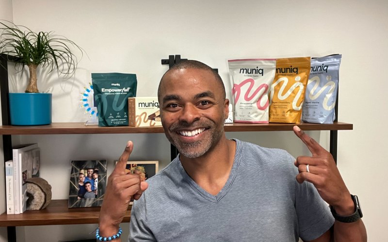 Muniq founder and CEO smiling and pointing to muniq shakes and new muniq products - empowerfull and bars