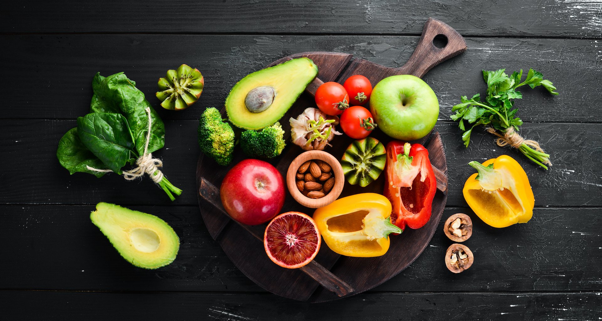 Fruits and vegetables containing fiber: Avocados, kiwi, apple, tomatoes, spinach, paprika, orange, lemon. Top view. Free space for your text. On a black background.